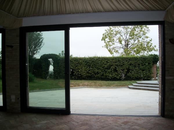 vetrata scorrevole con infissi in alluminio verniciato scuro e vista su giardino